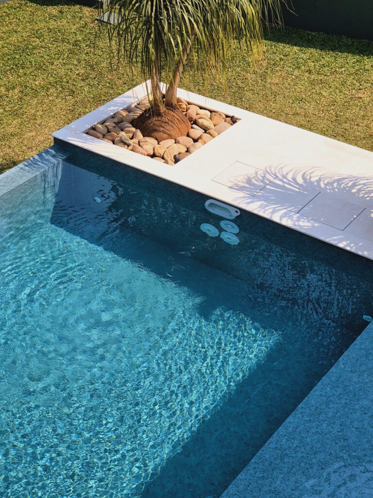 Uma piscina em formato de L com borda infinita em um quintal de uma casa - projeto-piscina-em-l-com-prainha-e-borda-infinita-curitiba