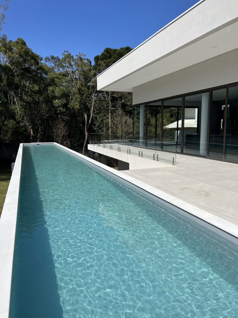 Uma piscina com raia na área externa de uma casa grande e moderna - projeto-de-piscina-raia-curitiba