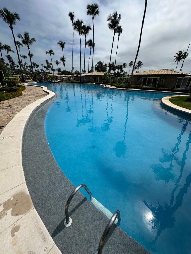 Uma piscina coletiva com árvores e pequenas casas ao redor localizada em um Resort no Nordeste - reforma-de-piscina-coletiva-em-resort