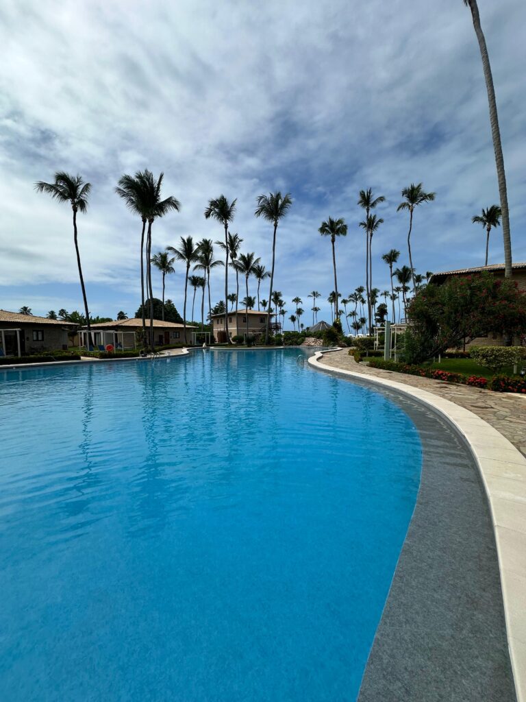 Uma piscina coletiva com árvores e pequenas casas ao redor localizada em um Resort no Nordeste - reforma-de-piscina-coletiva-em-resort