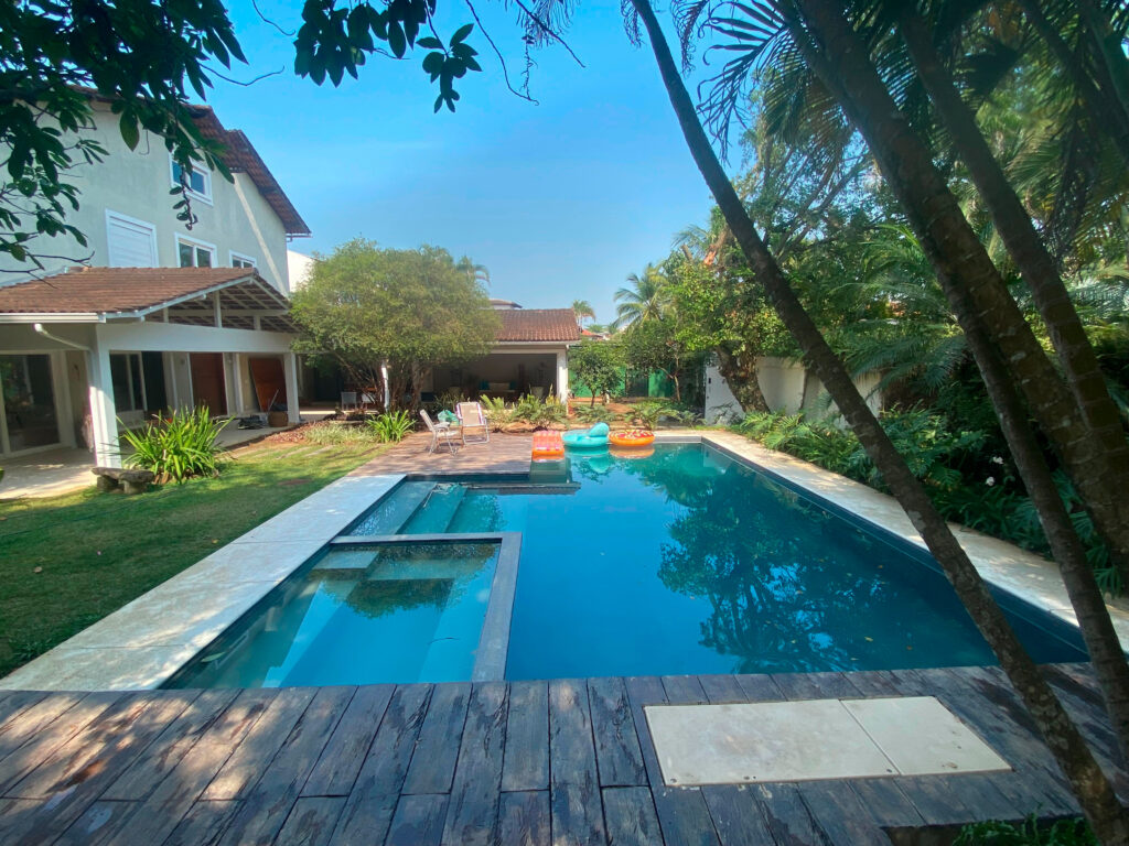 Quintal de uma casa com uma grande piscina reformada pela Desjoyaux ao redor é possível ver um jardim - reforma-de-piscina-rio-de-janeiro