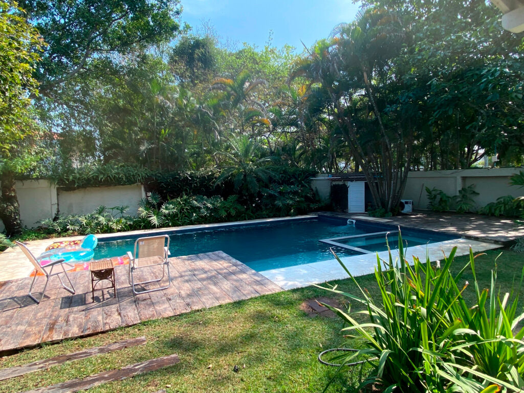 Quintal de uma casa com uma grande piscina reformada pela Desjoyaux ao redor é possível ver um jardim - reforma-de-piscina-rio-de-janeiro