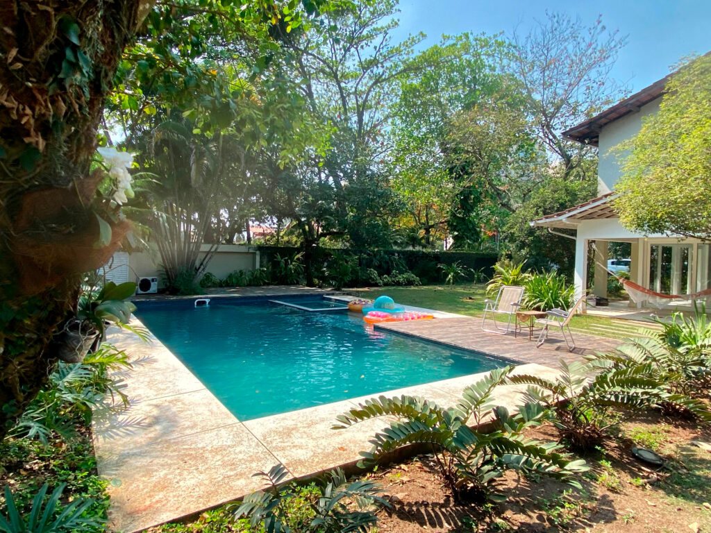 Quintal de uma casa com uma grande piscina reformada pela Desjoyaux ao redor é possível ver um jardim - reforma-de-piscina-rio-de-janeiro