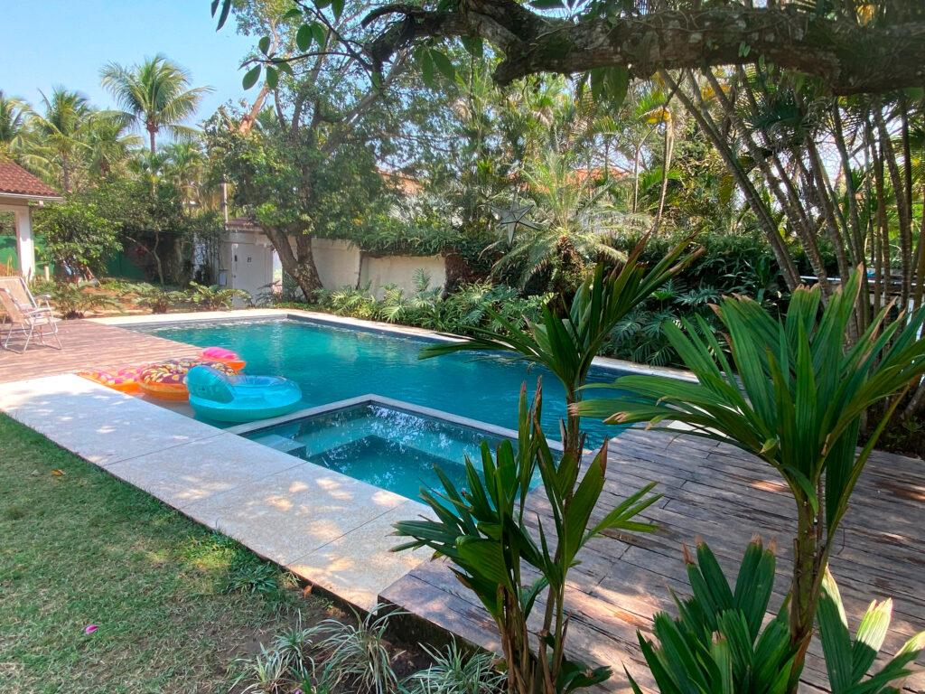 Quintal de uma casa com uma grande piscina reformada pela Desjoyaux ao redor é possível ver um jardim - reforma-de-piscina-rio-de-janeiro